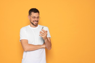 Photo of Happy man looking at smartphone on orange background. Space for text