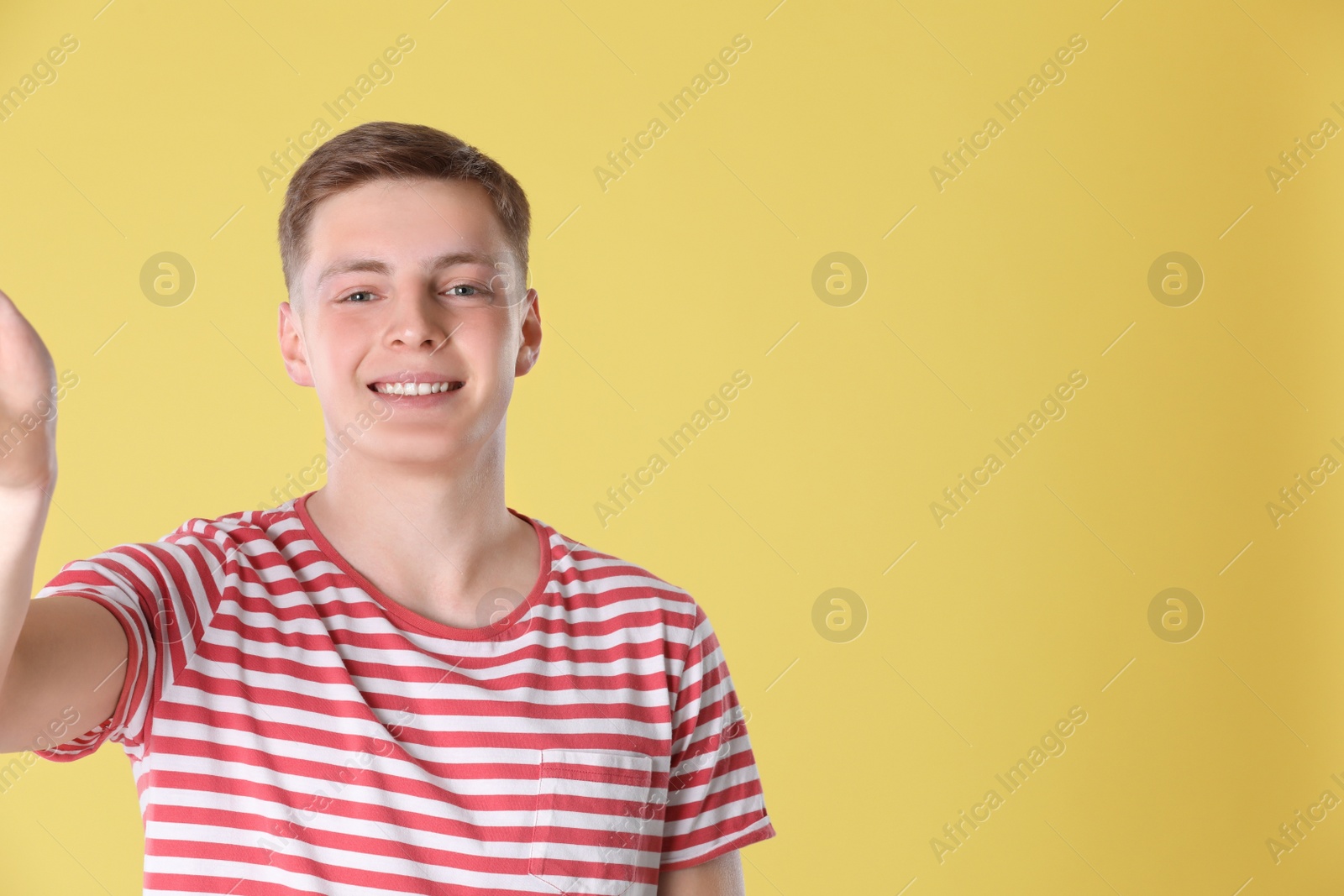 Photo of Happy teenage boy taking selfie on yellow background. Space for text