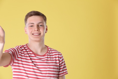 Photo of Happy teenage boy taking selfie on yellow background. Space for text