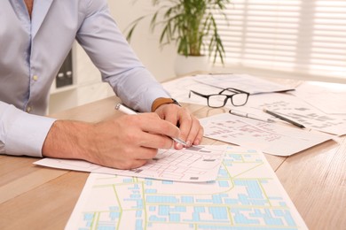 Professional cartographer working with cadastral map at wooden table in office, closeup