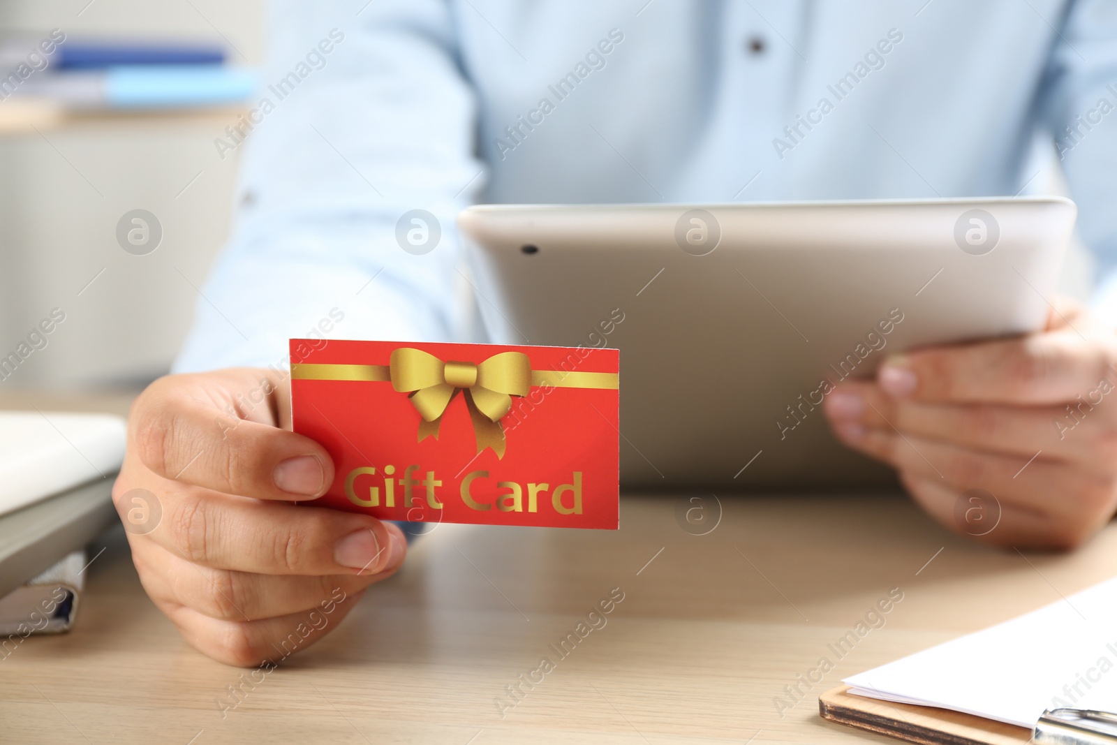 Photo of Man with gift card and tablet at table indoors, closeup