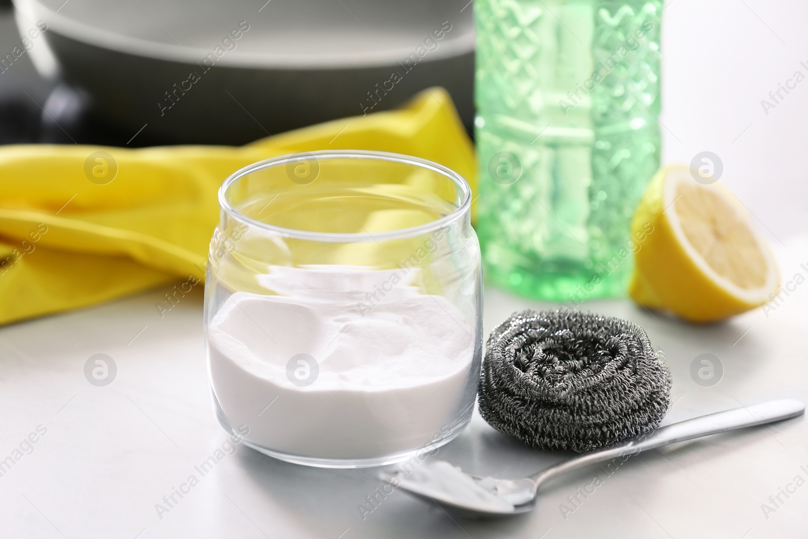 Photo of Baking soda, metal sponge and spoon on light stone table. Eco friendly detergent