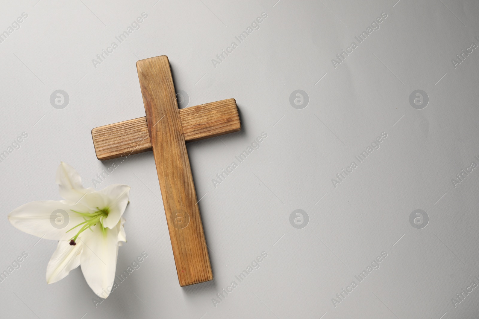 Photo of Wooden cross and lily flower on grey background, top view with space for text. Easter attributes