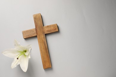 Wooden cross and lily flower on grey background, top view with space for text. Easter attributes