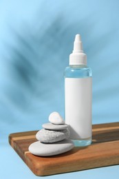 Cosmetic product, stacked stones and shadow of tropical leaf on light blue background