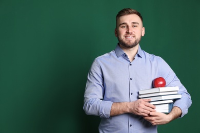 Portrait of young teacher with books and apple on green background. Space for text