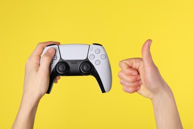 Photo of Woman with game controller showing thumbs up on yellow background, closeup