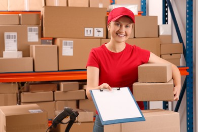 Photo of Post office worker with parcels and clipboard near rack indoors