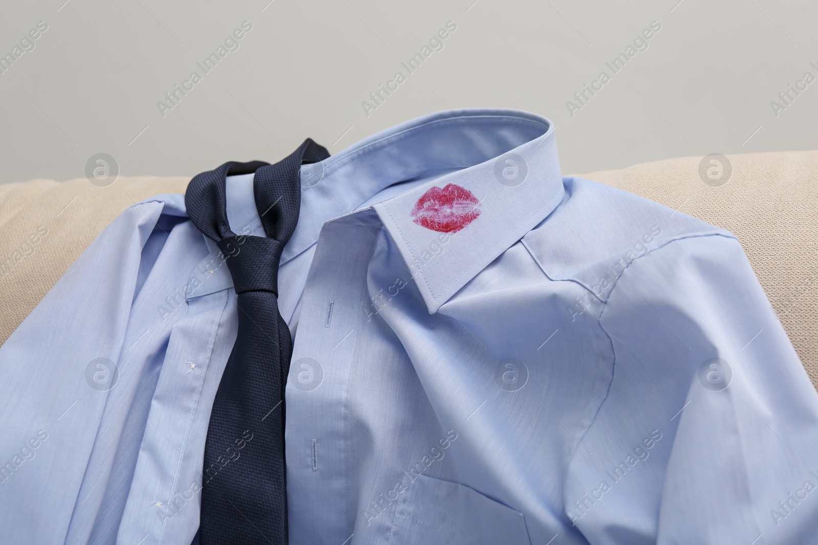 Photo of Men's shirt with lipstick kiss mark and necktie on sofa indoors