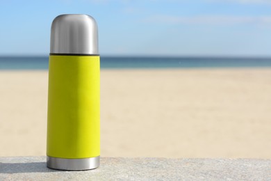 Photo of Metallic thermos with hot drink on stone surface near sea, space for text