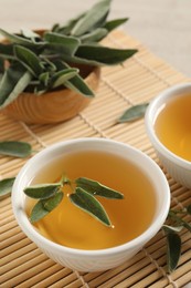 Photo of Cup of aromatic sage tea with fresh leaves on table