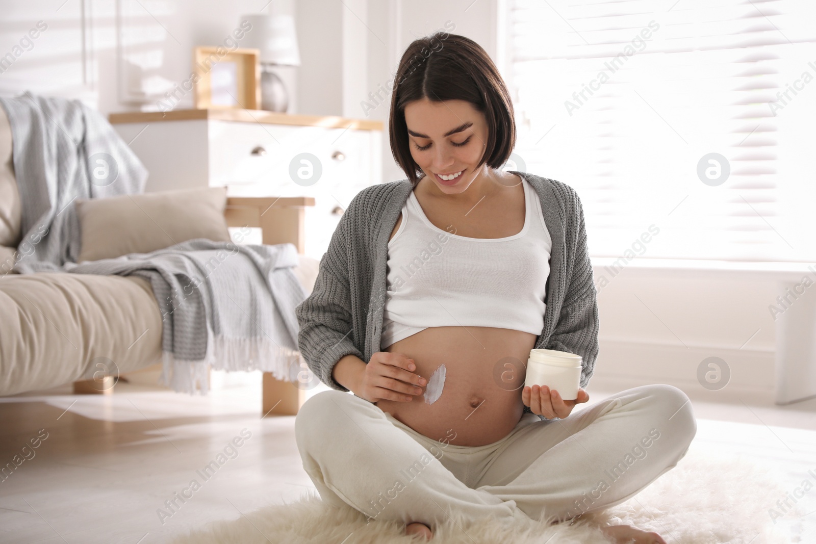 Photo of Young pregnant woman with cosmetic product at home