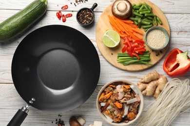 Flat lay composition with black wok and products on light wooden table