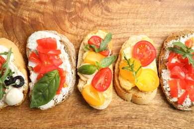 Delicious tomato bruschettas on wooden background, flat lay