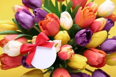 Photo of Bouquet of beautiful colorful tulips with blank card on yellow background, closeup. Birthday celebration