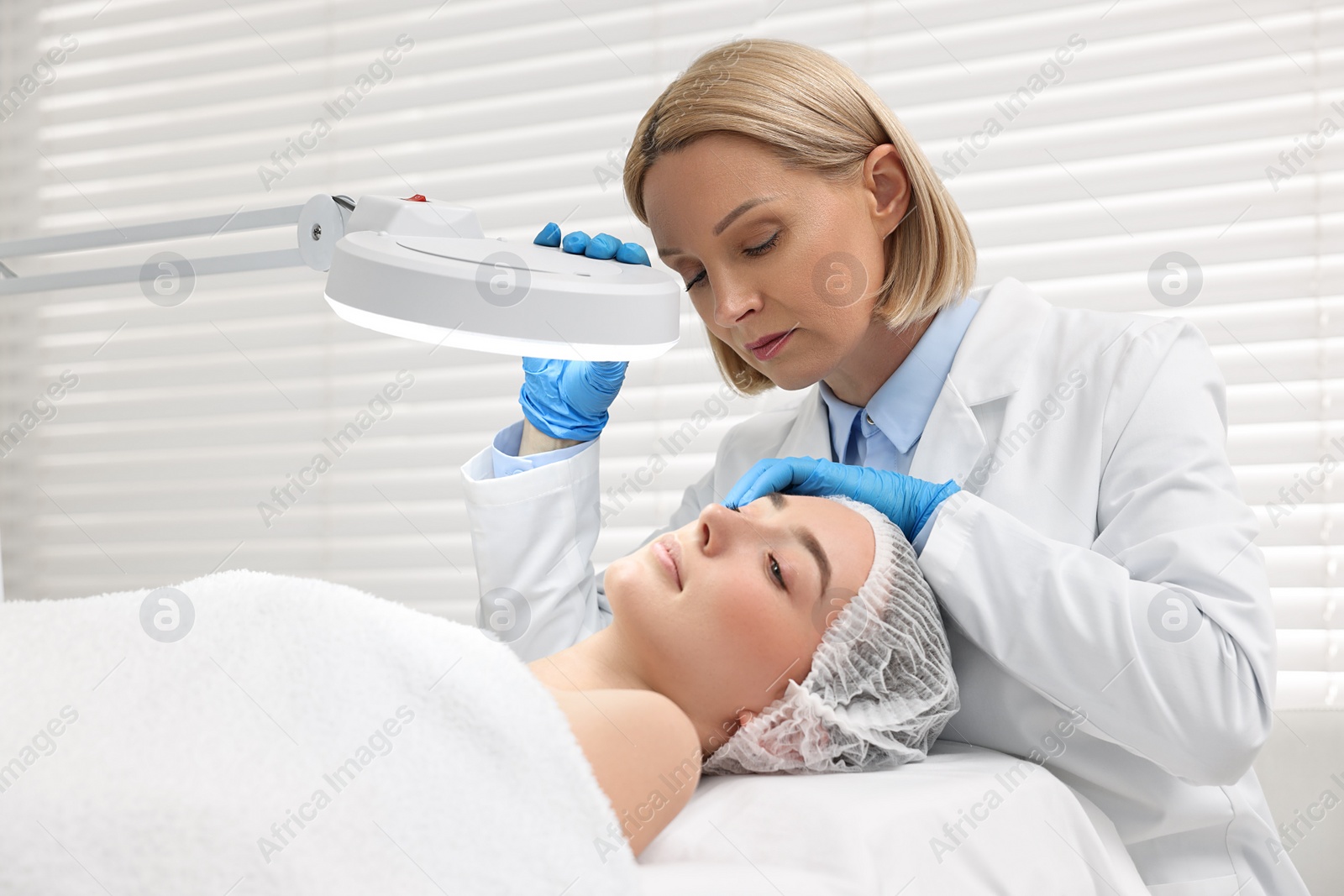 Photo of Dermatologist examining patient`s face under lamp in clinic