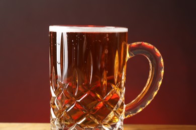 Photo of Mug with fresh beer on table against burgundy background, closeup