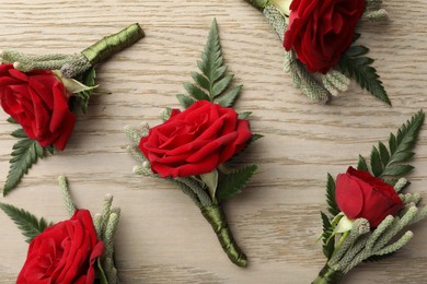 Many stylish red boutonnieres on light wooden table, flat lay