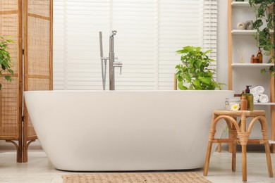 Photo of Spa day. Stylish bathroom interior with ceramic tub and green houseplants