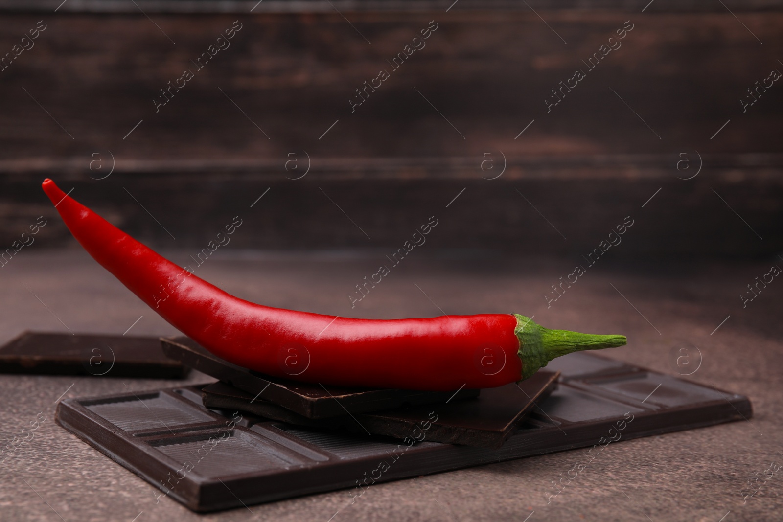 Photo of Delicious chocolate and fresh red chili pepper on grey textured table