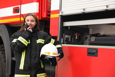 Photo of Firefighter in uniform using portable radio set near fire truck