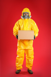 Man wearing chemical protective suit with cardboard box on red background. Prevention of virus spread