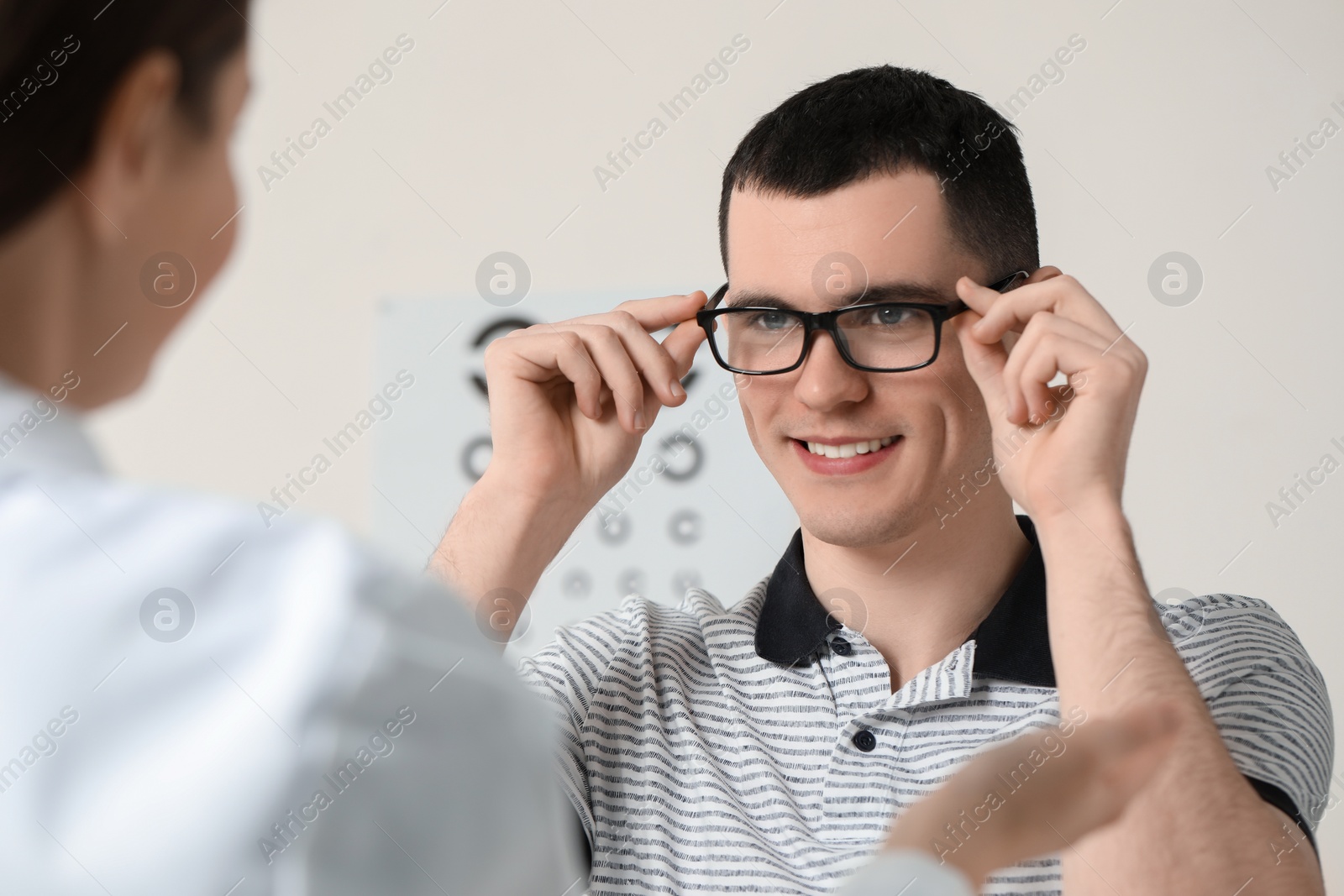 Photo of Vision testing. Ophthalmologist giving glasses to young man indoors