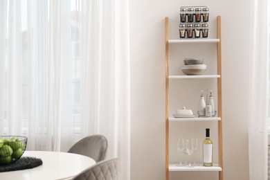 Stylish ladder shelf with kitchenware in dining room