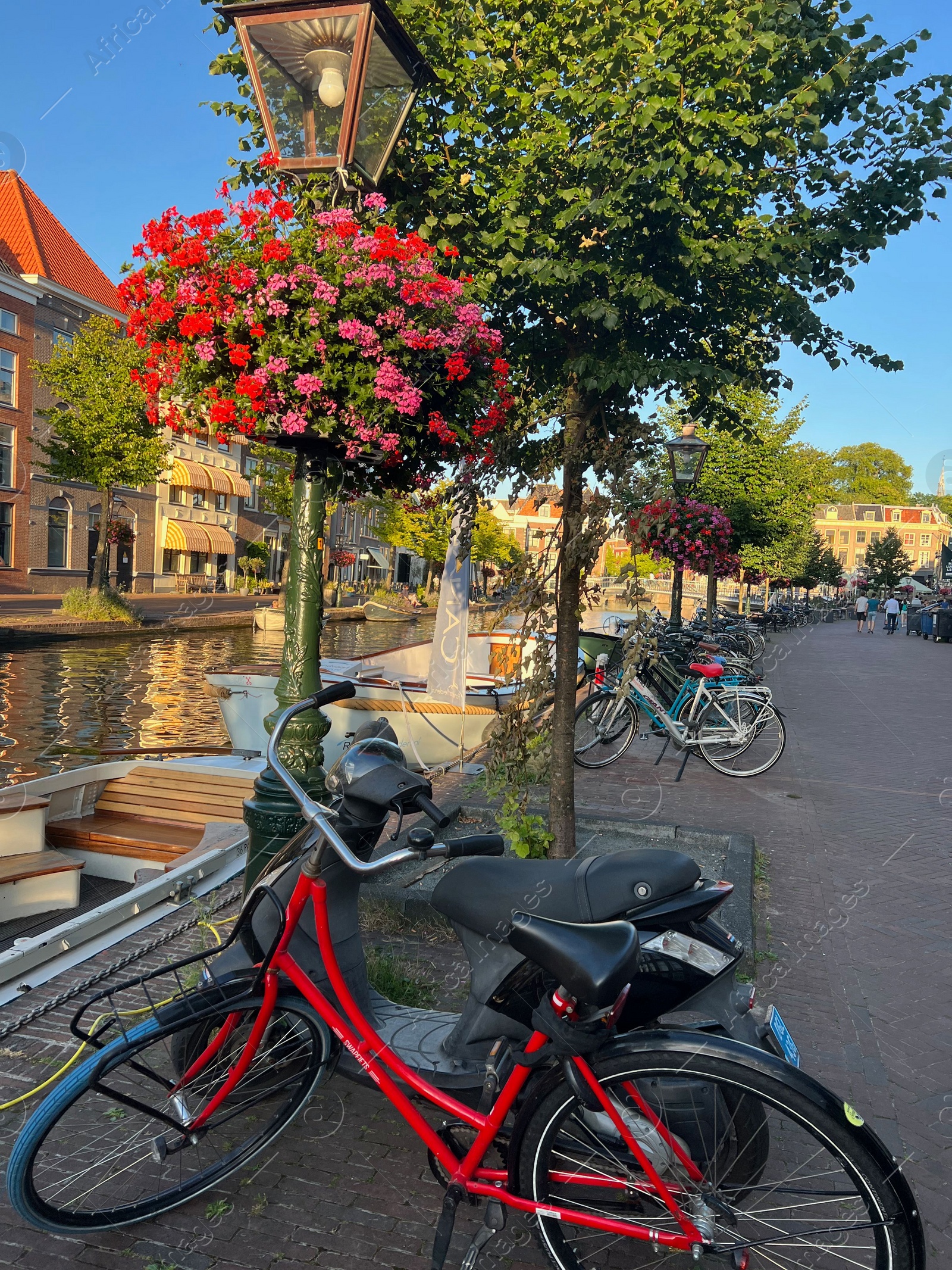 Photo of Leiden, Netherlands - August 1, 2022: Picturesque view of city canal with moored boats and parked bicycles