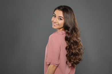 Beautiful woman with shiny wavy hair on grey background