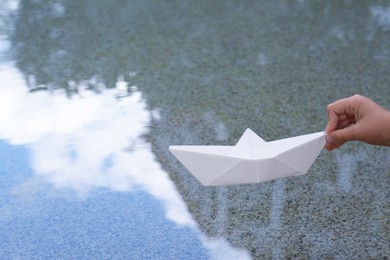 Photo of Kid launching small white paper boat on water outdoors, closeup
