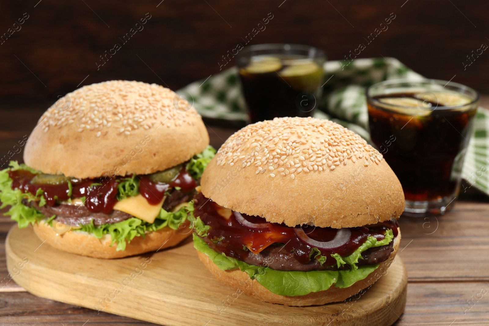 Photo of Board with delicious cheeseburgers on wooden table, closeup