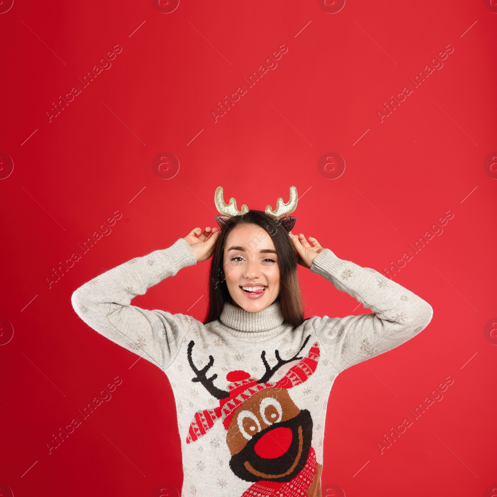 Photo of Young woman in Christmas sweater and deer headband on red background, space for text