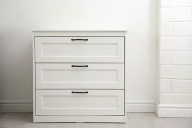 Photo of Modern white chest of drawers near light wall in room. Interior design