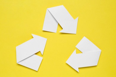 Photo of Recycling symbol made of white paper arrows on yellow background, top view