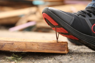 Photo of Careless worker stepping on nails in wooden plank outdoors, closeup