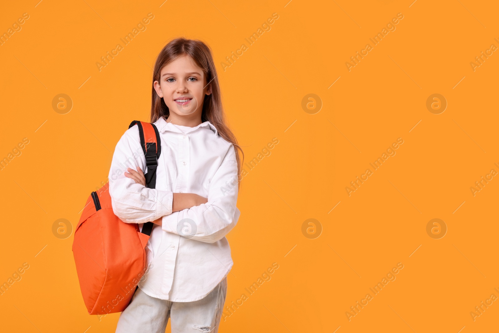 Photo of Happy schoolgirl with backpack on orange background. Space for text