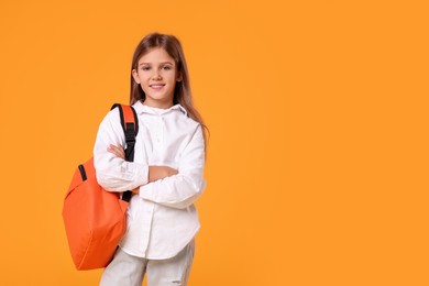 Photo of Happy schoolgirl with backpack on orange background. Space for text