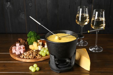 Photo of Fondue pot with melted cheese, glasses of wine and different products on wooden table