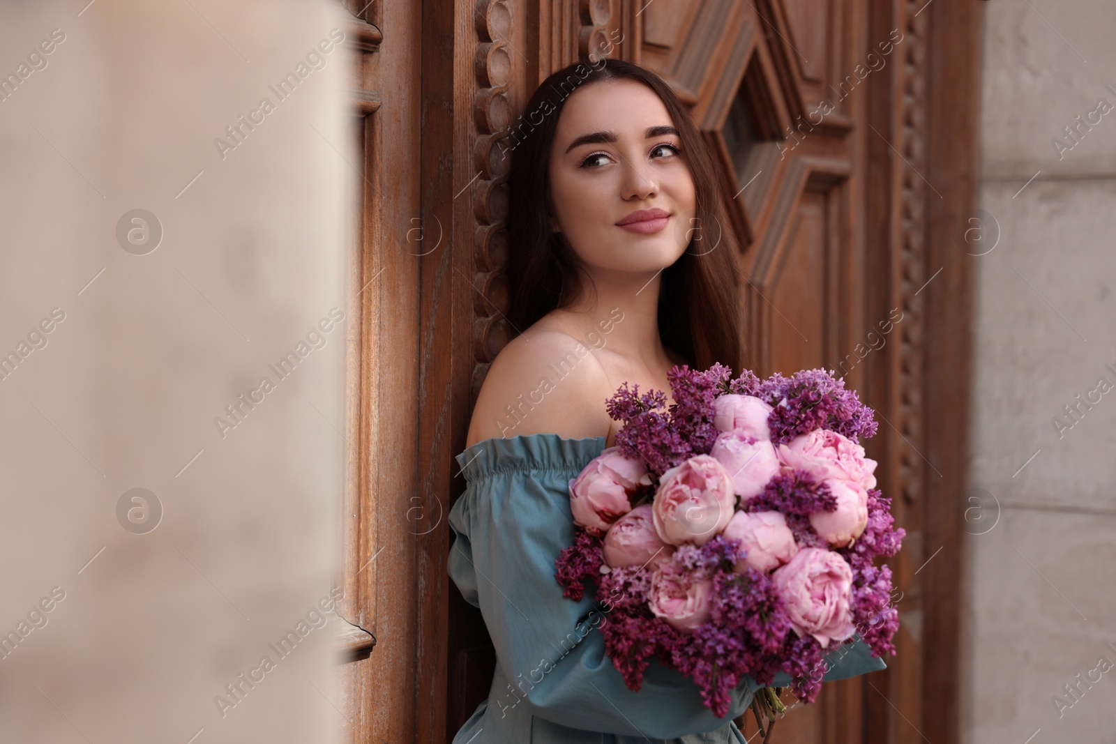 Photo of Beautiful woman with bouquet of spring flowers near building outdoors, space for text