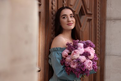 Photo of Beautiful woman with bouquet of spring flowers near building outdoors, space for text