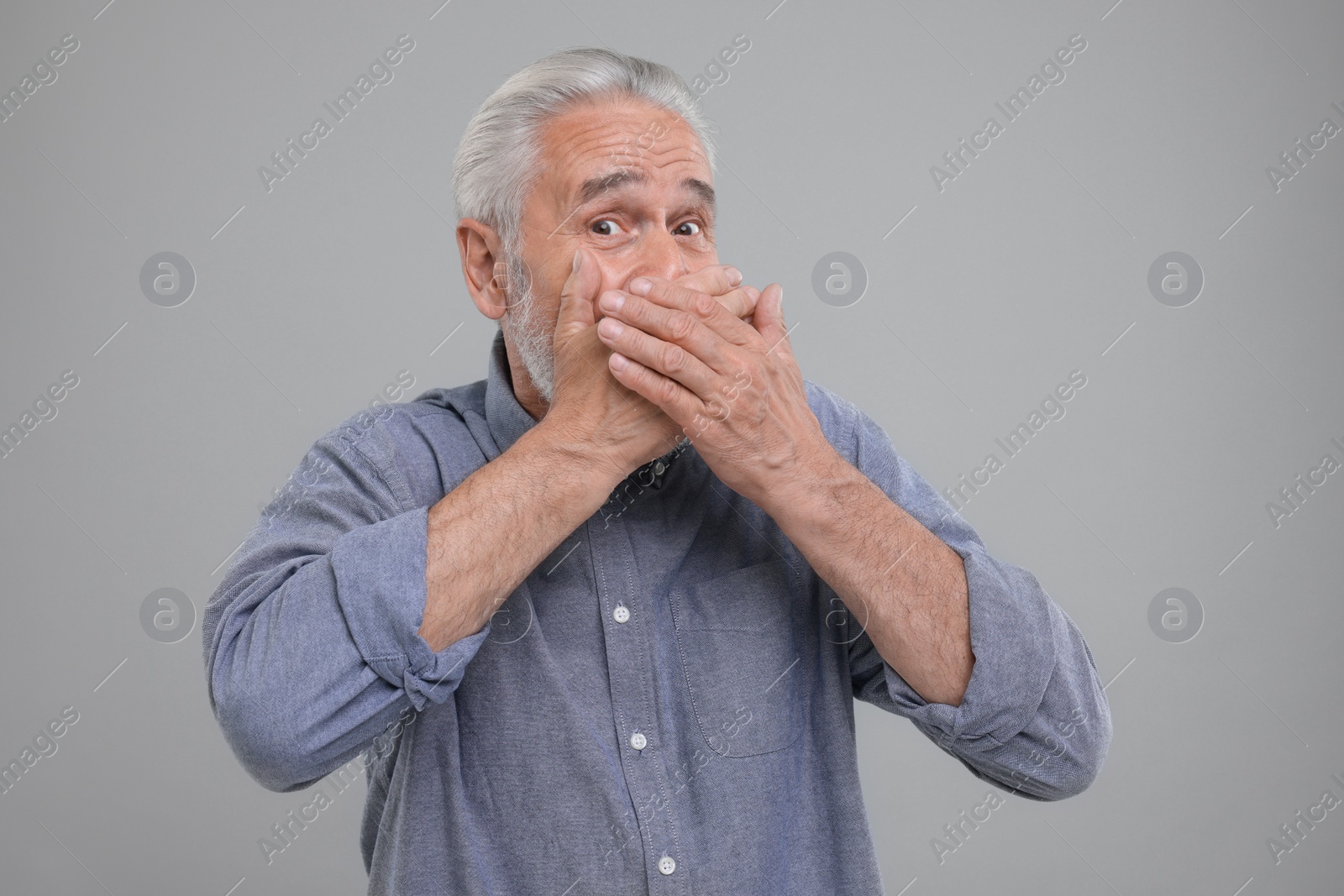 Photo of Embarrassed senior man covering mouth with hands on light grey background