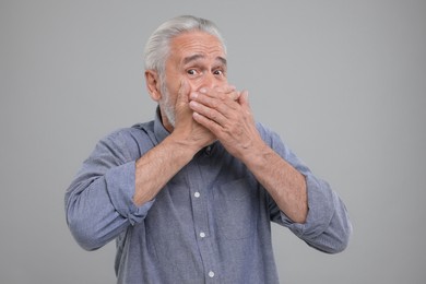 Photo of Embarrassed senior man covering mouth with hands on light grey background