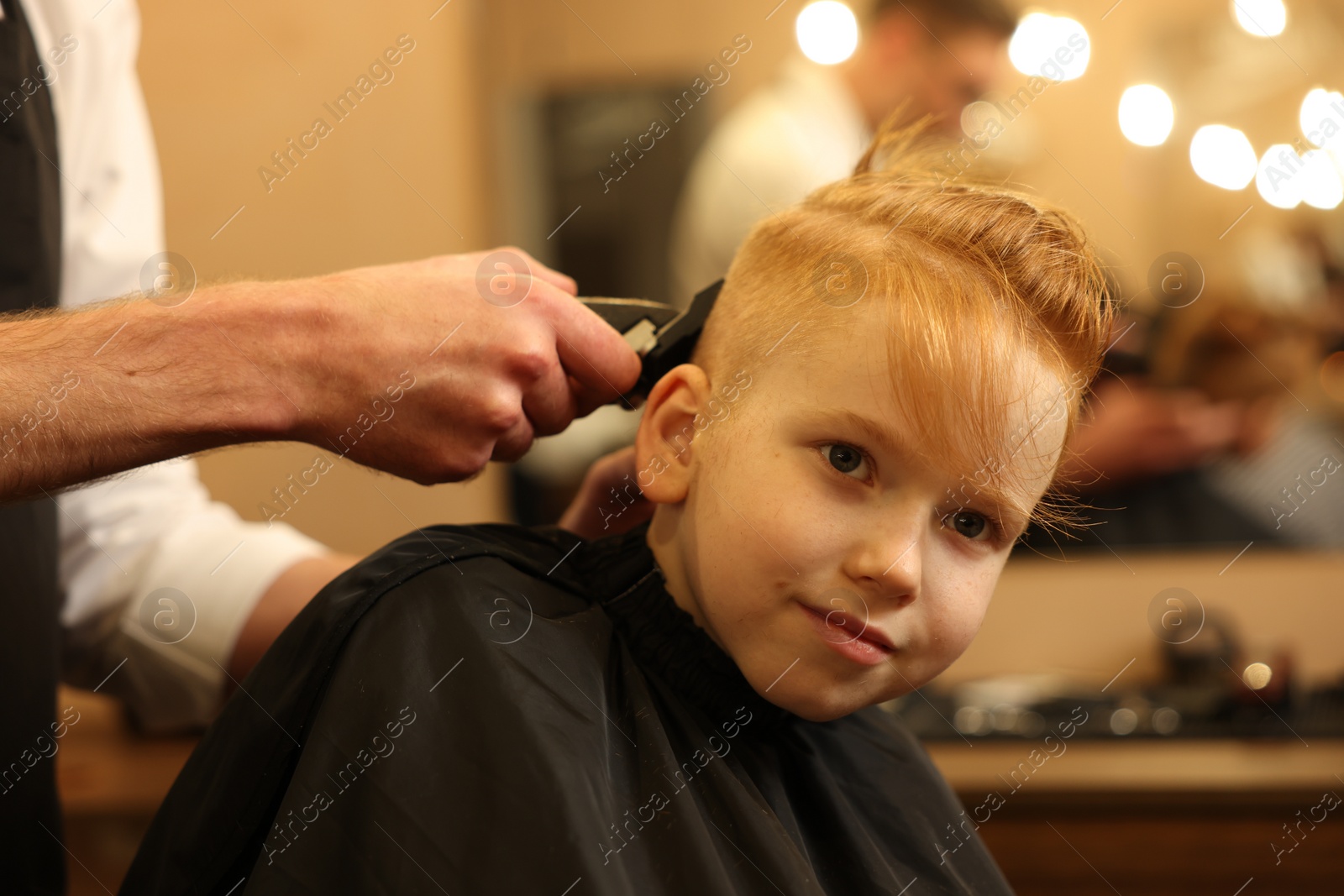 Photo of Professional hairdresser cutting boy's hair in beauty salon, closeup