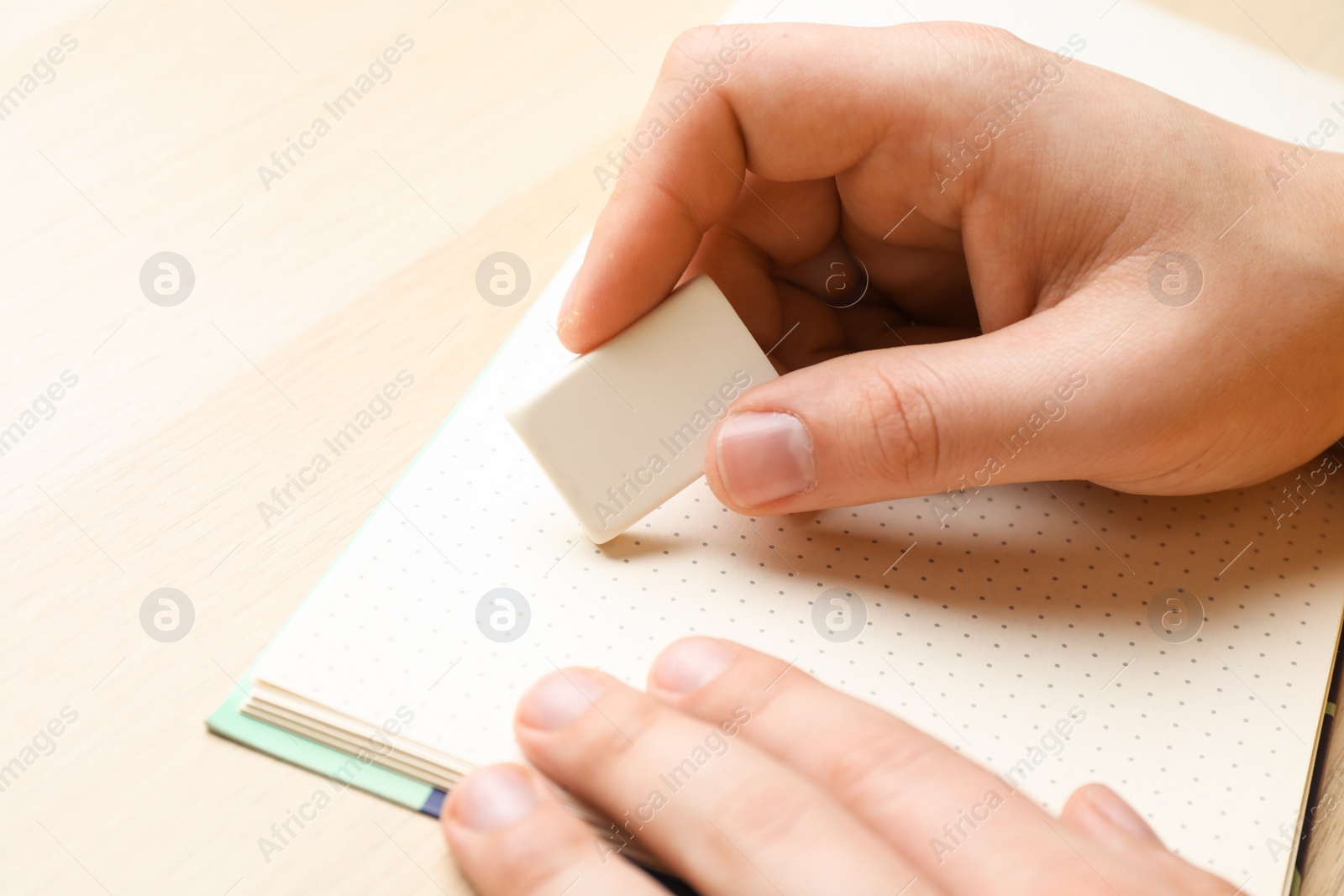 Photo of Man erasing something in notebook at wooden table, closeup