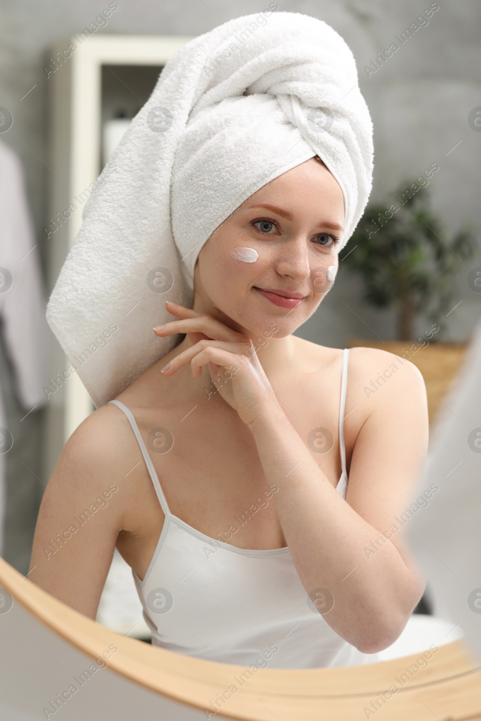 Photo of Beautiful woman with freckles and cream on her face near mirror in bathroom