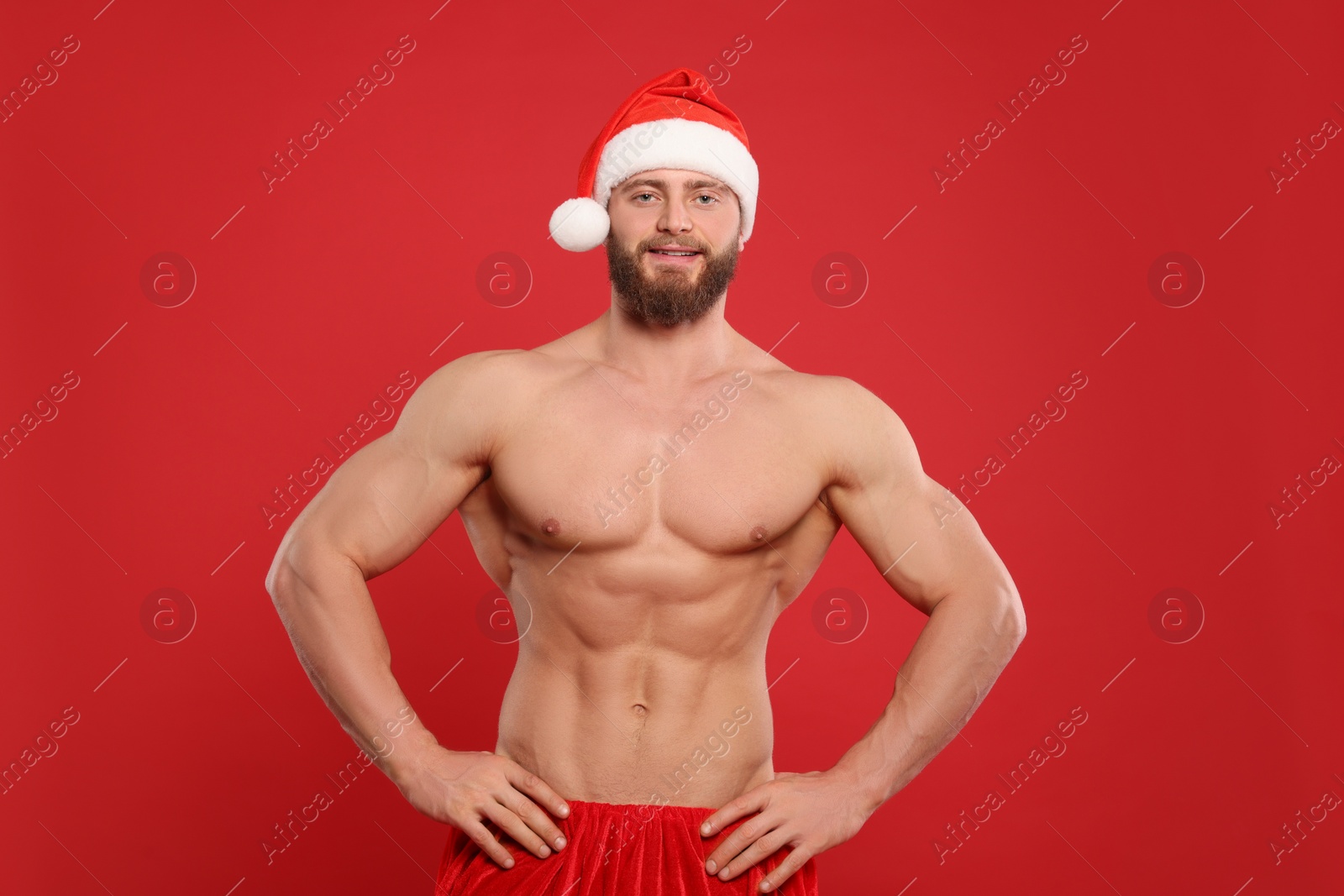 Photo of Muscular young man in Santa hat on red background