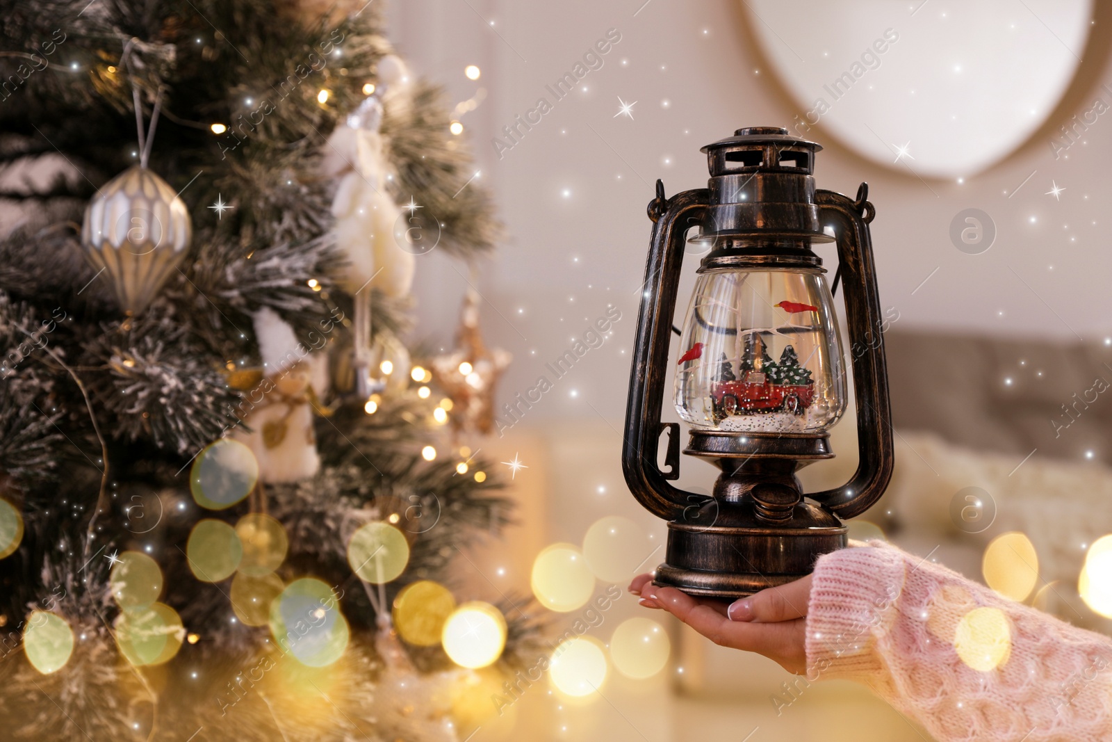 Image of Woman holding snow globe in vintage lantern near Christmas tree at home, closeup