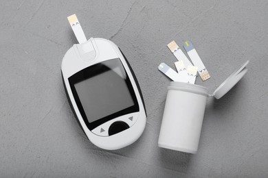 Photo of Glucometer and bottle with strips on grey table, flat lay. Diabetes testing kit
