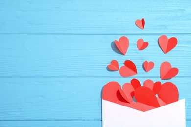 Photo of Envelope with small paper hearts on wooden background, top view